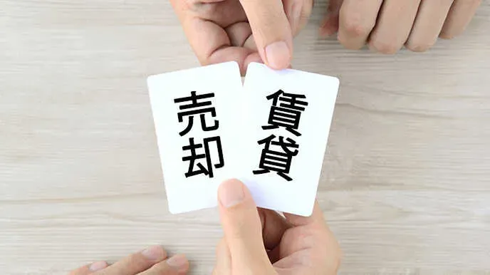 賃貸と売却の文字が書かれた二枚のカードを手に持って比較する様子。