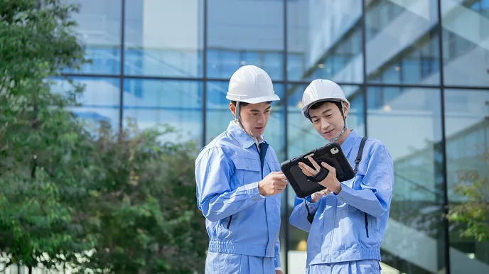 一棟マンションやビルの管理に関する相談をイメージした、作業服を着たスタッフが建物前でタブレットを確認している様子の写真。