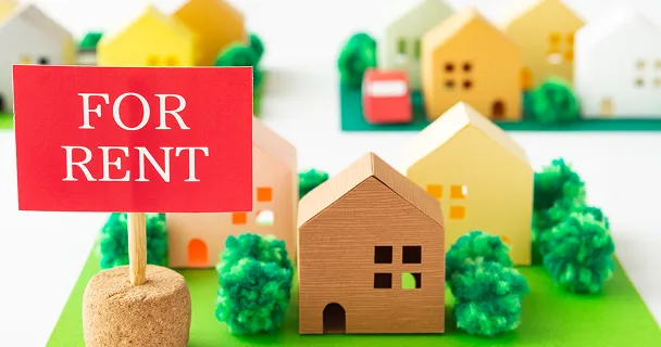 FOR RENT の看板と家の模型が並ぶ、不動産賃貸をイメージした写真。